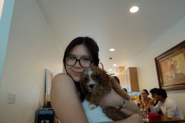 A woman in glasses holding a small curly-haired dog